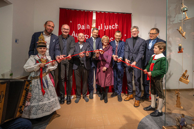 Inaugurazione simbolica della nuova mostra sui giocattoli Sevi con il taglio del nastro rosso, tenuto da scolari in costume tradizionale gardenese, 4.12.2025.  Da destra a sinistra: i direttori del Dipartimento Innovazione, Ricerca, Università e Musei Franz Schöpf e Manuel Gatto, il direttore del Dipartimento Cultura ladina Mathias Stuflesser con l’assessore provinciale Daniel Alfreider, la direttrice del museo Paulina Moroder e il presidente Georg Senoner, i sindaci di Ortisei e Santa Cristina Tobia Moroder e Christoph Senoner.